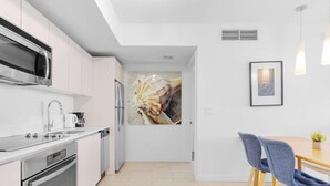 A modern kitchen with stainless steel appliances, a white countertop, and a dining area with a table and chairs. - Modern Upscale 1BR, Bay & Marina View, Resort Pool (Hallandale Beach)