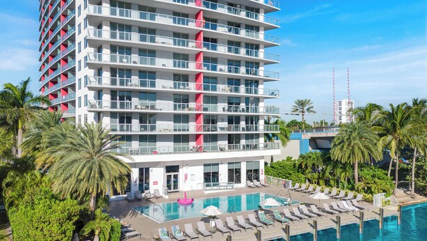 A multi-story hotel with a rooftop pool, palm trees, and a clear blue sky. - Modern Upscale 1BR, Bay & Marina View, Resort Pool (Hallandale Beach)