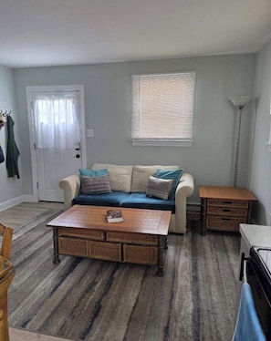 A living room with a sofa, a coffee table, a floor lamp, and a door with a window. - Charming 1-bedroom apartment with AC in Brigantine (Brigantine)