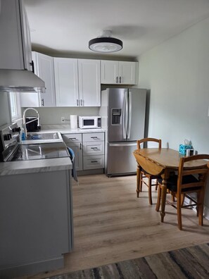 A modern kitchen with white cabinets, a stainless steel refrigerator, a microwave, and a wooden dining table with chairs. - Charming 1-bedroom apartment with AC in Brigantine (Brigantine)