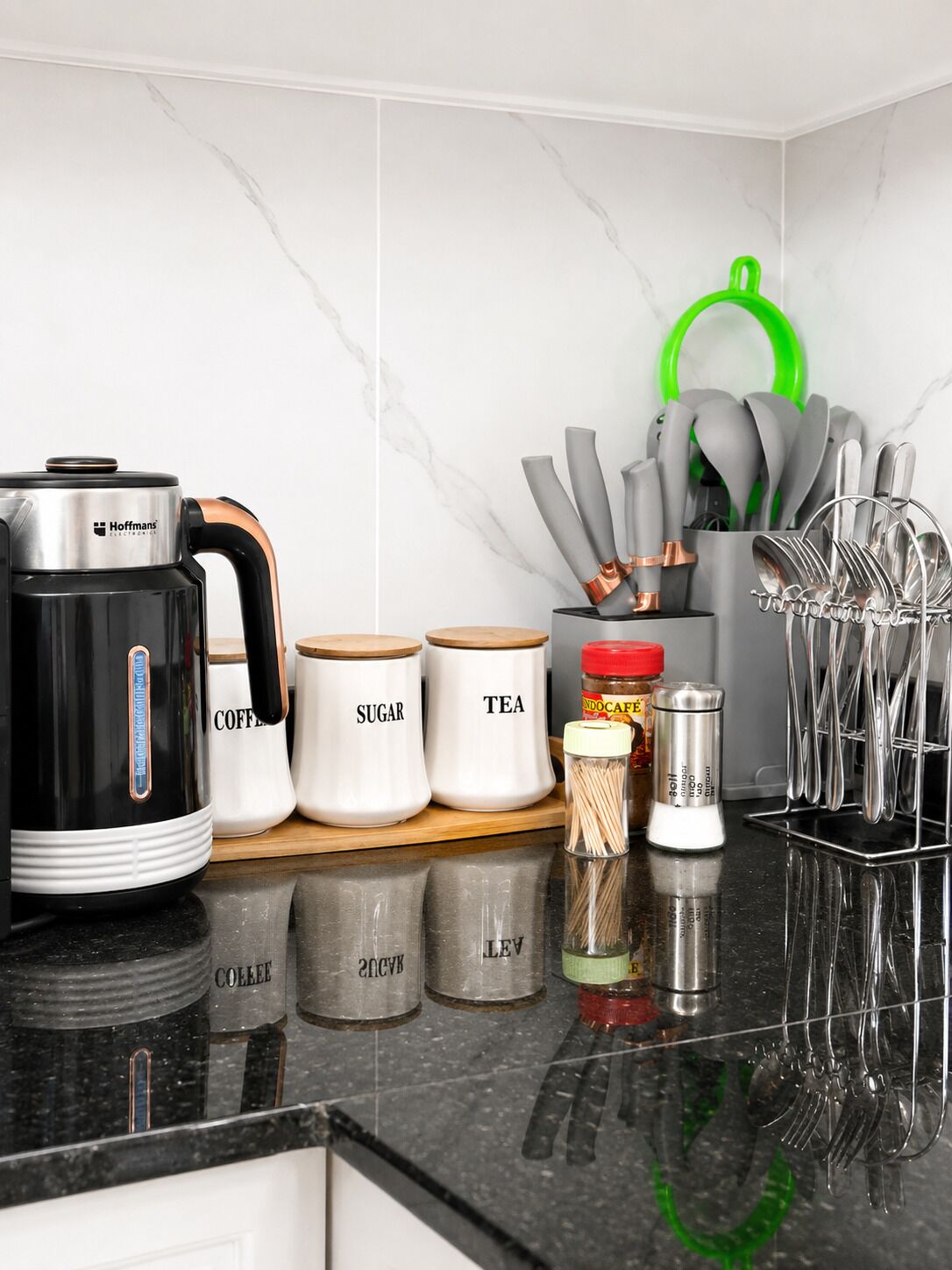 Una encimera de cocina con cafetera, azúcar, recipientes de té, frascos de especias y un portalapices.