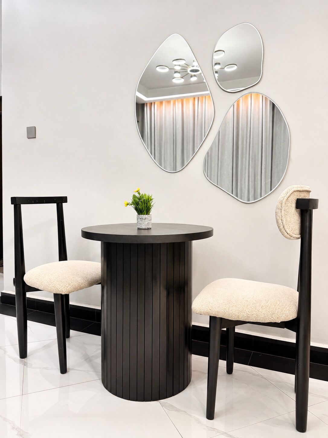 A modern interior with a round table, two chairs, and decorative wall mirrors.