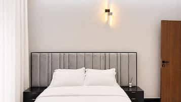A modern bedroom with a bed, nightstands, a wall-mounted light fixture, and a wooden door.