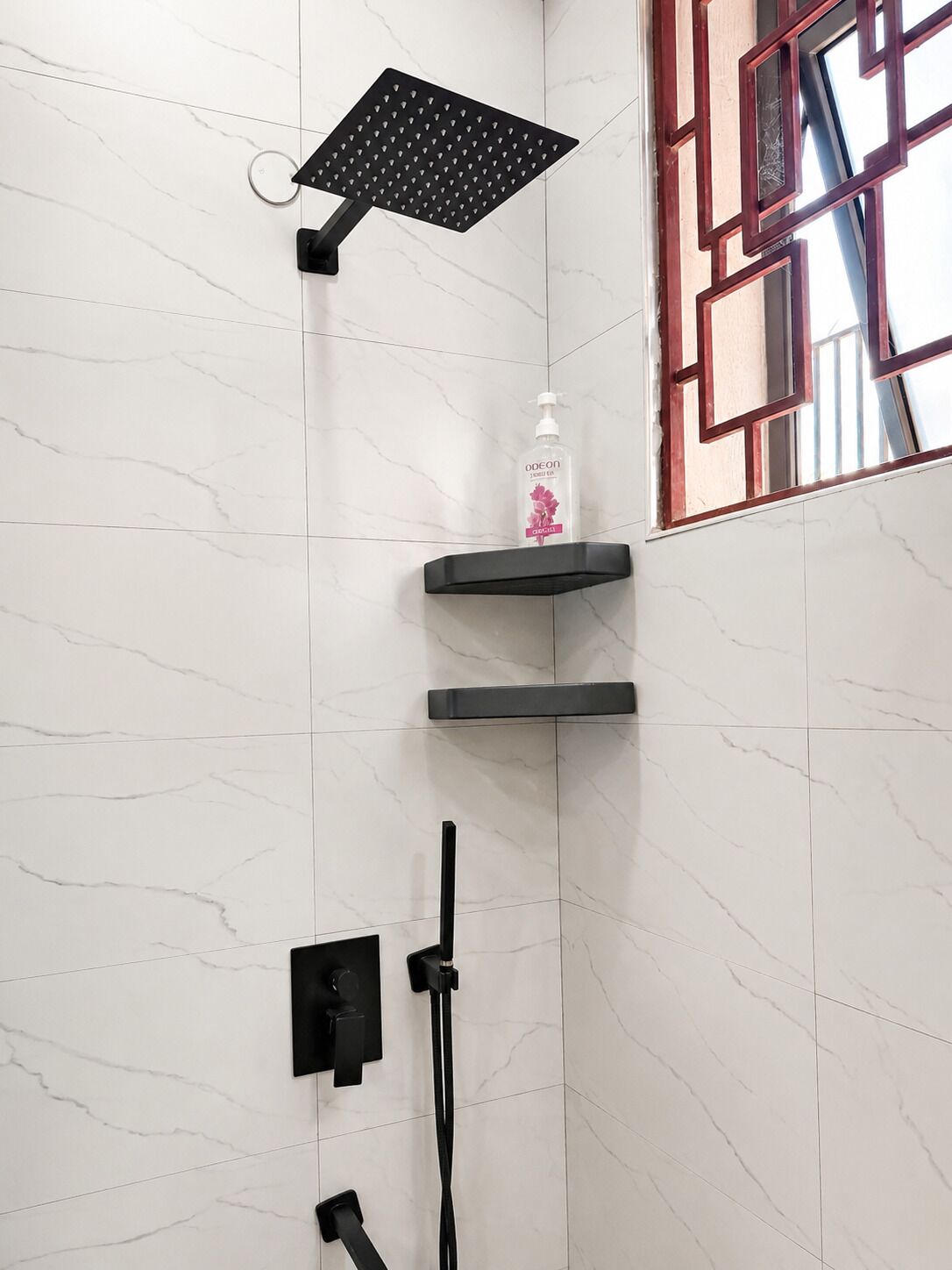 A bathroom with a shower, a soap dispenser, and a window with a geometric frame.