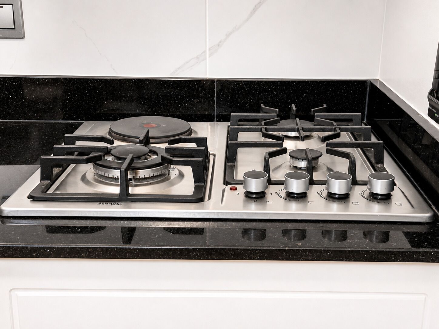 A kitchen with a gas stove, a range hood, and a black countertop.