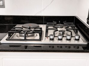 Une cuisine équipée d’une cuisinière à gaz, d’une hotte aspirante et d’un plan de travail noir.