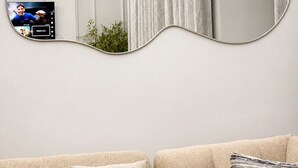 A modern living room with a unique curved mirror, a television displaying a live stream, and a sofa with cushions.