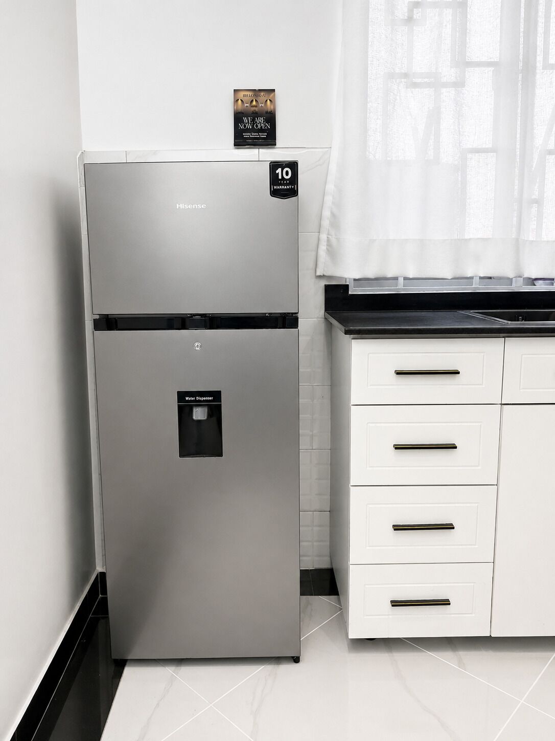 A kitchen with a stainless steel refrigerator, a water dispenser, and white cabinetry.