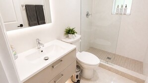Een moderne badkamer met een wit wastafelmeubel, toilet en een douchecabine van glas, plus een kleine pot met een plantje.