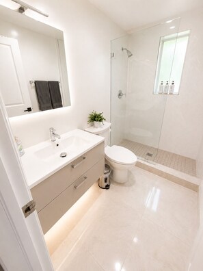 A modern bathroom with a white sink, a toilet, a glass shower enclosure, and a small potted plant. - Beautiful studio with 2 beds- Midtown (Miami)