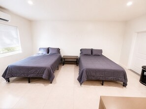 A room with two beds, a small table, and a trash bin. - Beautiful studio with 2 beds- Midtown (Miami)