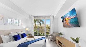 A hotel room with a bed, a desk, a chair, and a large window with a view of palm trees and a sunset. - Cozy 1BR- Bay View - Resort Pool & Private Balcony (Hallandale Beach)