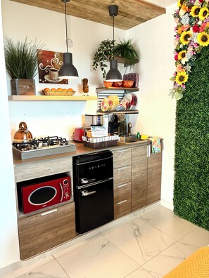 Una cucina moderna con piano cottura integrato, lavastoviglie nera e forno a microonde. Sono presenti mobili in legno, un lampadario e uno scaffale a parete con oggetti decorativi.