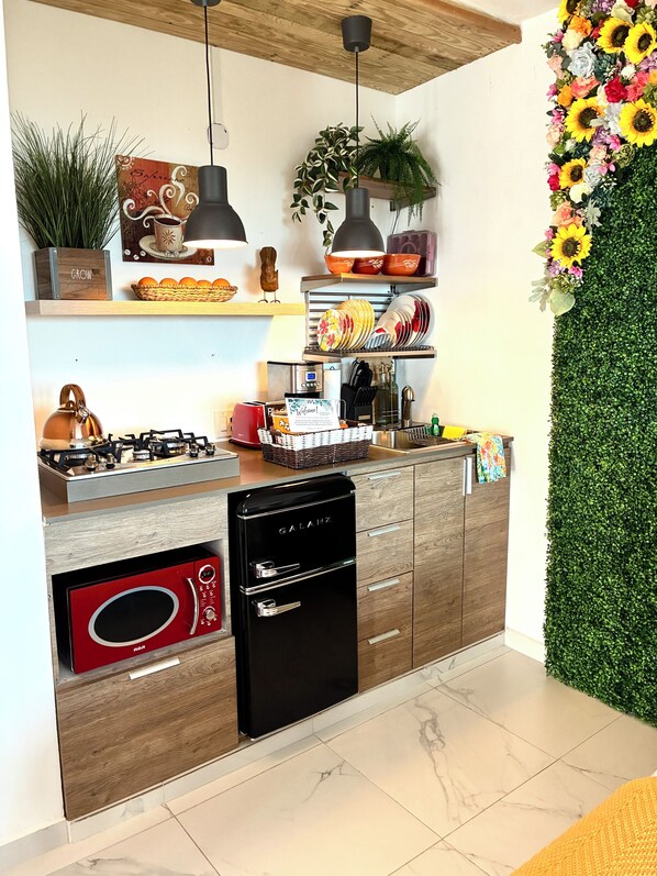 A modern kitchen with a built-in stove, a black dishwasher, and a microwave. There are wooden cabinets, a hanging light fixture, and a wall-mounted shelf with decorative items.