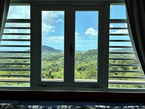 A room with a large window offering a view of a green landscape and hills.