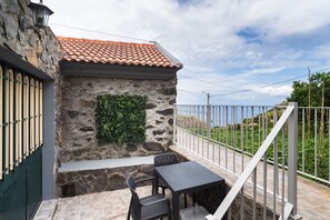 A stone building with a tiled roof, a metal railing, and a table with chairs. - GuestReady - Charming Getaway in Ribeira da Janela (Ribeira da Janela)