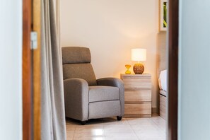 A room with a grey armchair, a wooden nightstand with a lamp, and a bed with white bedding. - GuestReady - Charming Getaway in Ribeira da Janela (Ribeira da Janela)