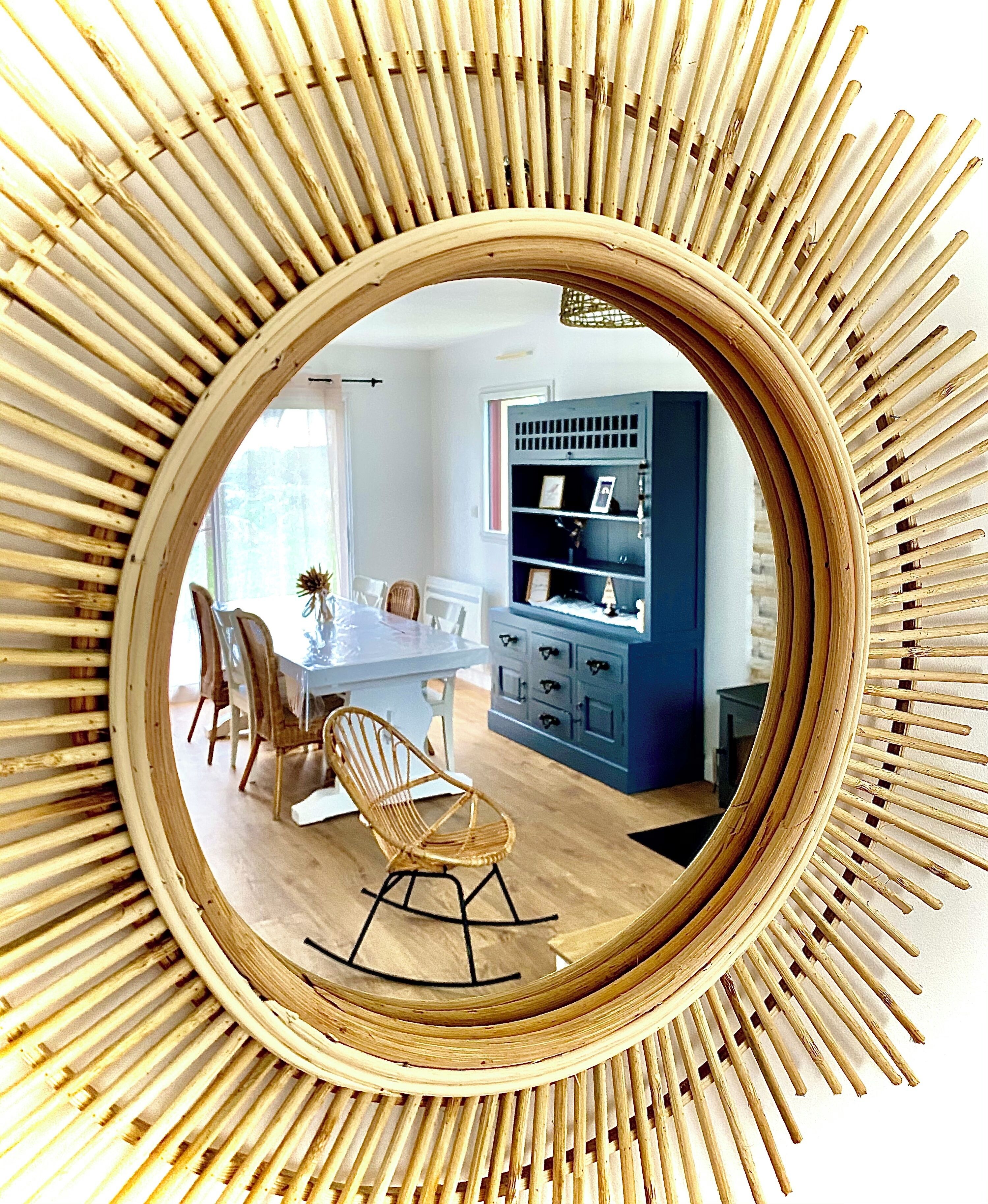 A dining area with a round mirror, wooden chairs, a table, and a blue cabinet with shelves.
