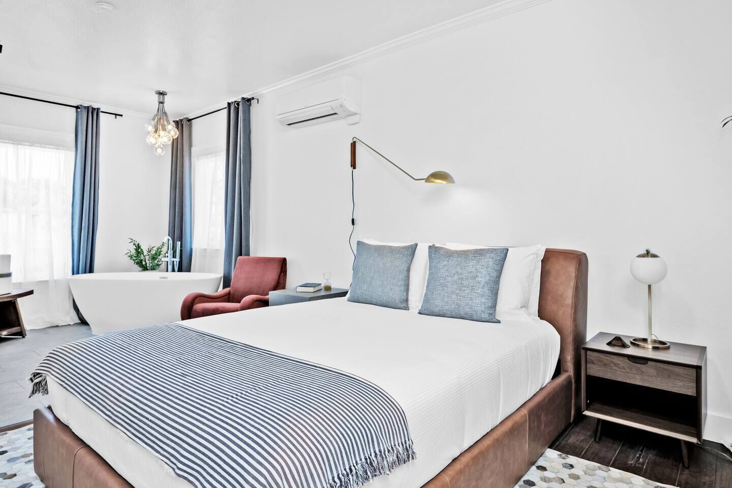 A modern hotel room with a large bed, a desk, a chair, and a bedside table with a lamp.