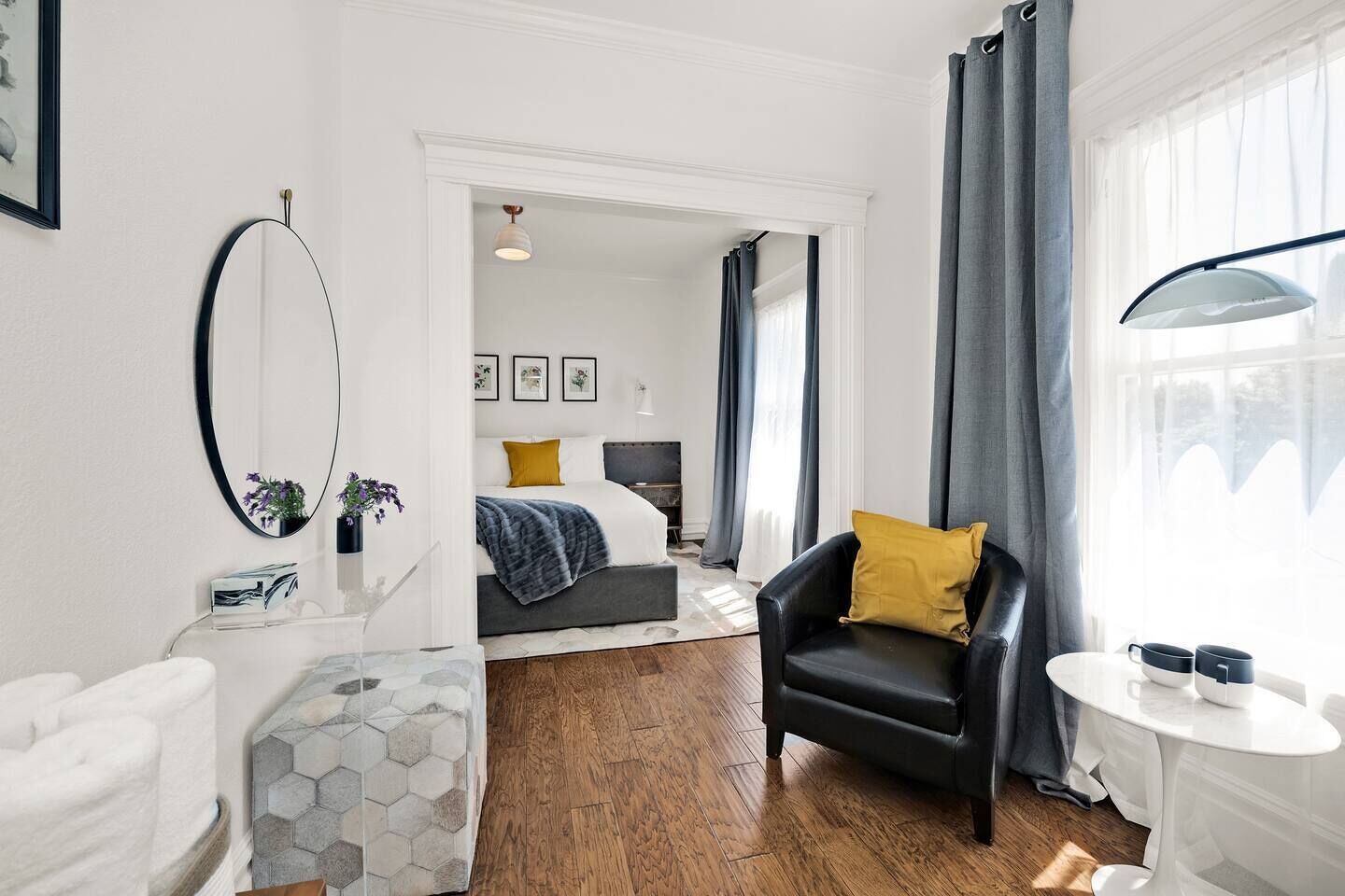 A modern hotel room with a bed, a chair, a table, and a large window with curtains.