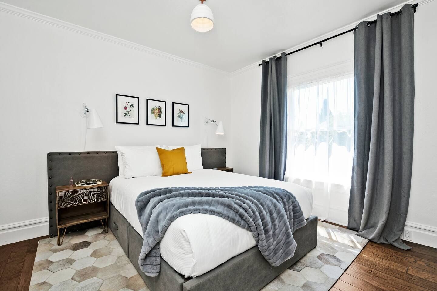 Et moderne soveværelse med en stor seng, et natbord, en lampe og udsigt over byen gennem vinduet.