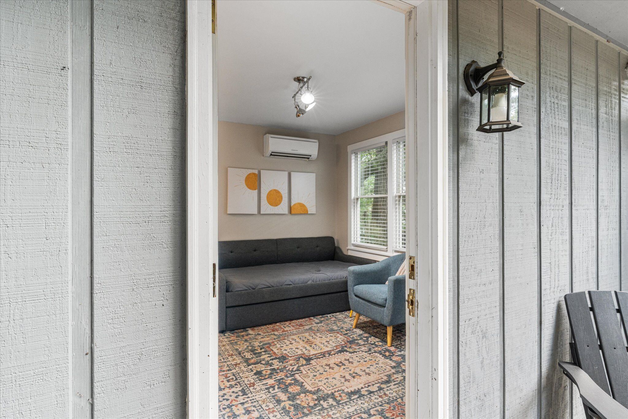 Un couloir avec un canapé gris, un tapis à motifs et une chaise bleue.