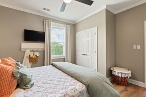 Une chambre à coucher avec un lit, une télévision, une fenêtre avec des rideaux, une porte et une table de chevet.