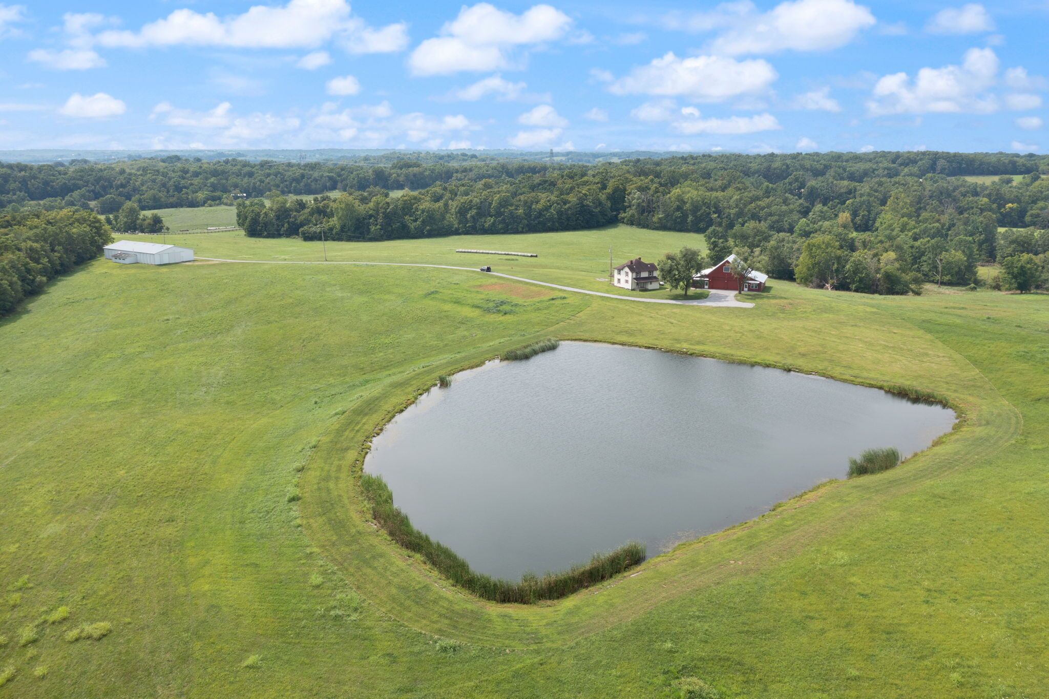 A large pond surrounded by green fields and a few buildings.