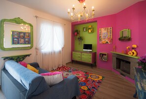Ein Zimmer mit einer Couch, einem Fernseher, einem Kamin und einem farbenfrohen Teppich.