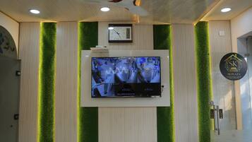 A reception area with a wall-mounted clock, a digital display with multiple camera feeds, and a logo for SK Plaza.