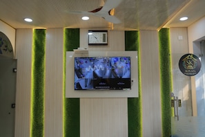 Zona de recepción con un reloj de pared, una pantalla digital con varias transmisiones de cámaras y el logotipo de SK Plaza.
