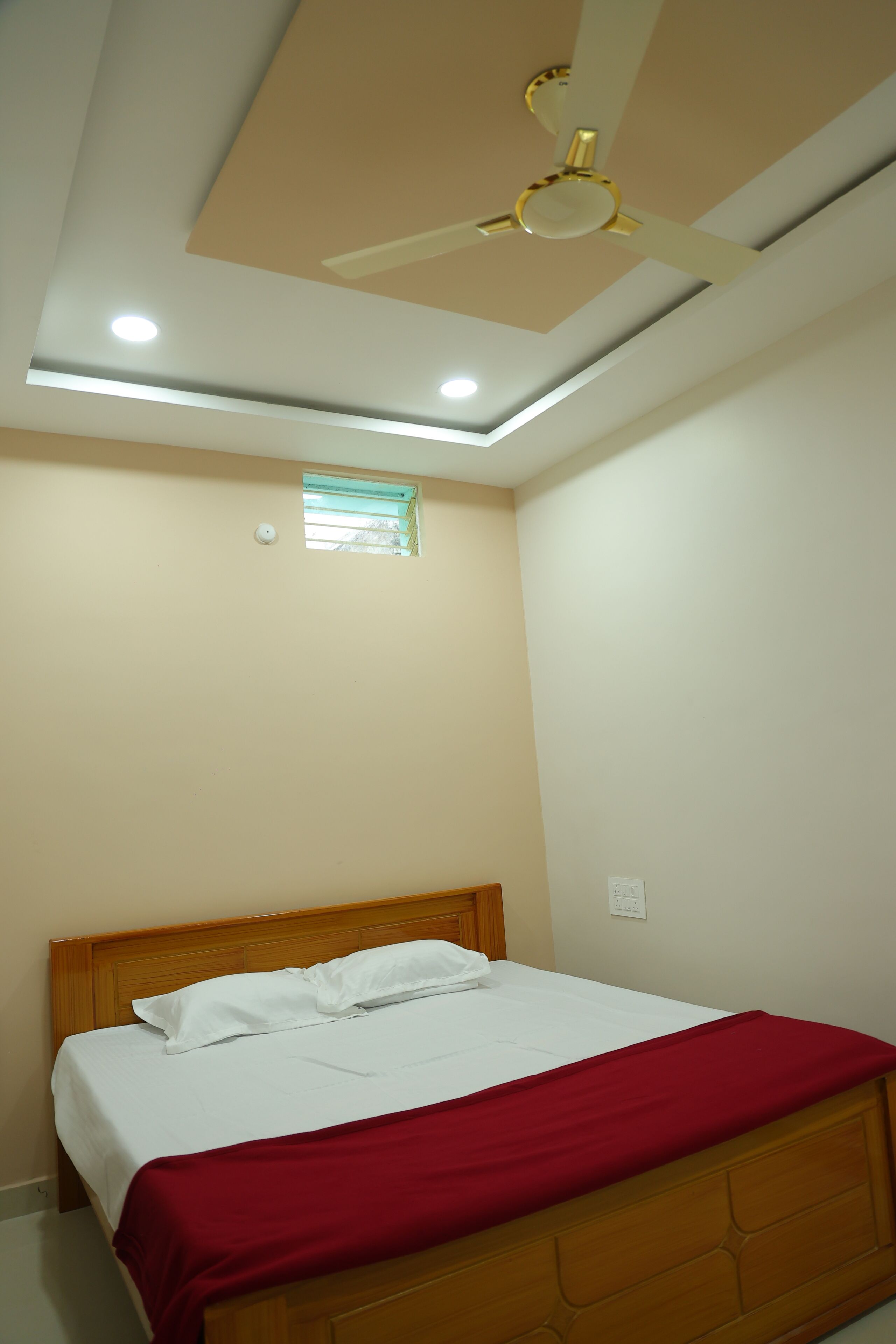 A bedroom with a bed, a ceiling fan, recessed lighting, a small window, and a wall-mounted light switch.