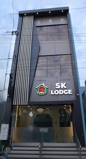 A modern building with a prominent SK Lodge sign, featuring a logo with a red 'SK' and a laurel wreath.