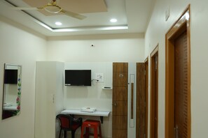 A room with a desk, chair, television, wardrobe, and a ceiling fan.