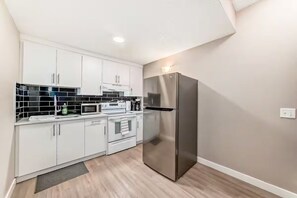Una cocina moderna con armarios blancos, un refrigerador de acero inoxidable, un microondas y una estufa.