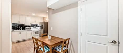 A compact kitchen with white cabinets, a dining table with chairs, and a white door.