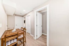 A dining area with a wooden table and chairs, a white door, and a hallway leading to another room. - NEW 5BR Home, FREE Private Parking, Entire House (Calgary)