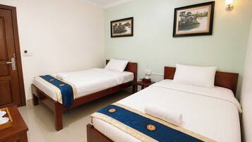 A hotel room with two beds, a wooden door, a small table, and two wall-mounted paintings.