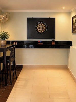 Una habitación con un dardo en la pared, una mesa con sillas y una planta en maceta.
