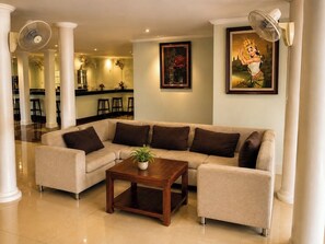 A living room with a sectional sofa, a coffee table, and a painting on the wall. - Abode Hotel Siem Reap (Siem Reap)