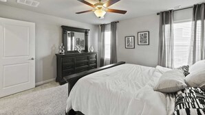 Ein Schlafzimmer mit Bett, Schminktisch, Deckenventilator und Fenster mit Vorhängen.