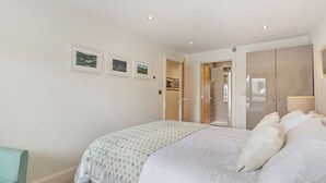 A bedroom with a large bed, a door leading to a bathroom, and three framed pictures on the wall. - Monkstone View - Direct Beach Access (Saundersfoot)