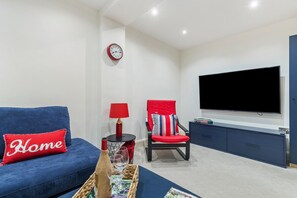 Un salon moderne avec un canapé bleu, un fauteuil rouge, un téléviseur à écran plat et une petite table d’appoint avec une lampe.