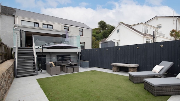 A modern outdoor patio with a dining area, a grassy lawn, and a black fence. - Monkstone View - Direct Beach Access (Saundersfoot)