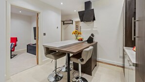 A modern kitchen with a wooden countertop, bar stools, a built-in oven, and a hanging pot rack. - Monkstone View - Direct Beach Access (Saundersfoot)