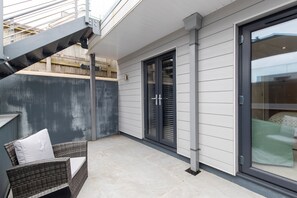 Ein überdachter Patio-Bereich mit Korbstuhl, einer Schiebetür aus Glas und einer Metalltreppe.