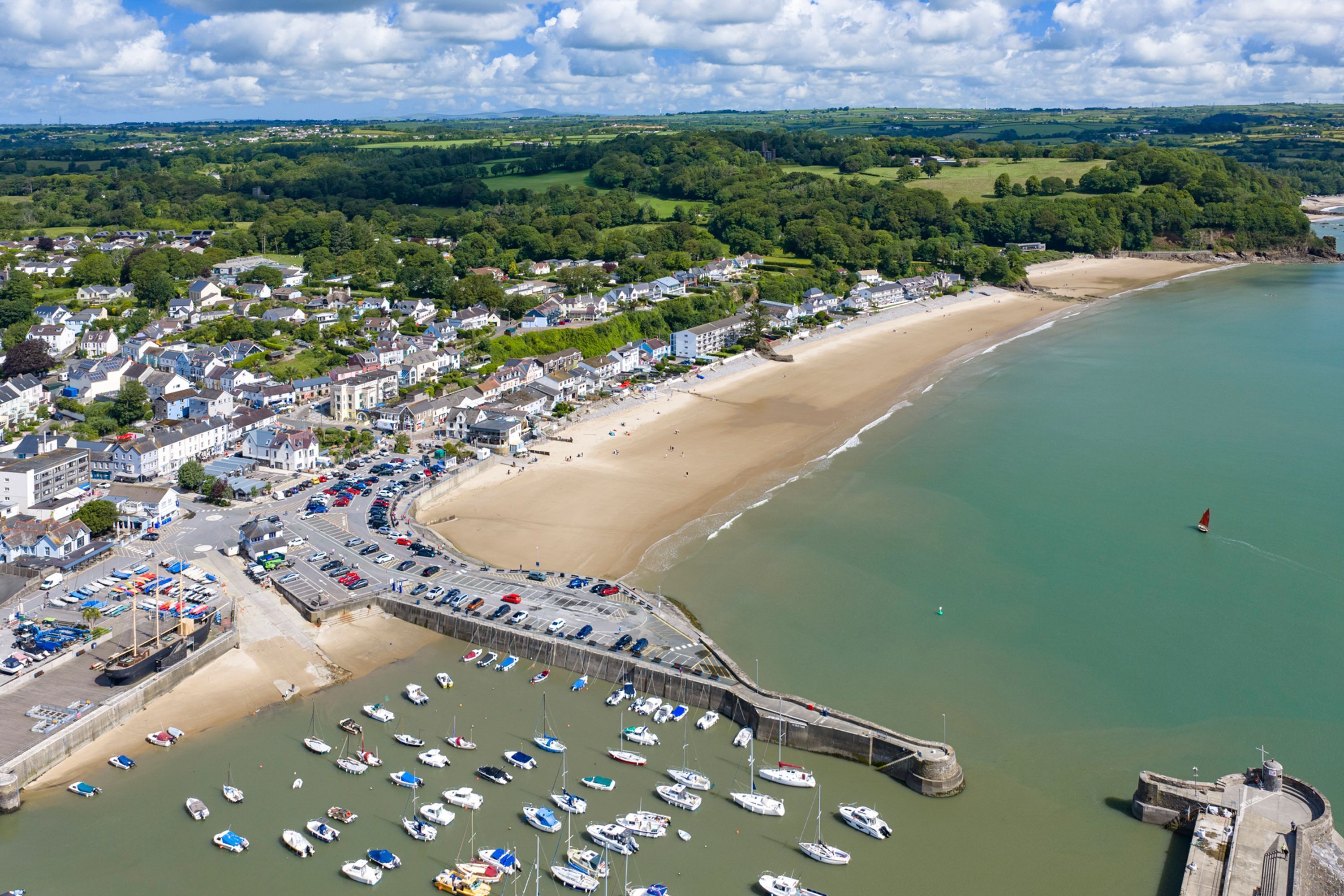 A coastal town with a sandy beach, a marina with numerous boats, and a fortified structure.