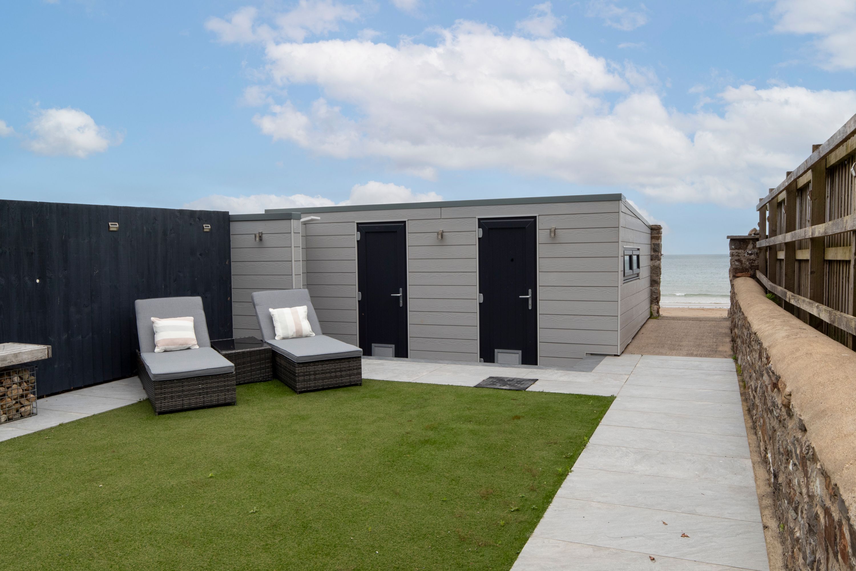 Un espace de détente extérieur moderne, doté de deux portes, d’une petite fenêtre et d’un coin salon avec des coussins.