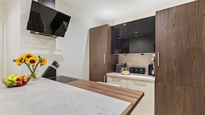 A modern kitchen with a built-in oven, a microwave, and a large black TV mounted on the wall. - Monkstone View - Direct Beach Access (Saundersfoot)