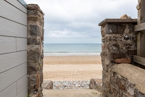 Une vue sur la plage, encadrée par une arche en pierre qui mène à un bâtiment en bois.